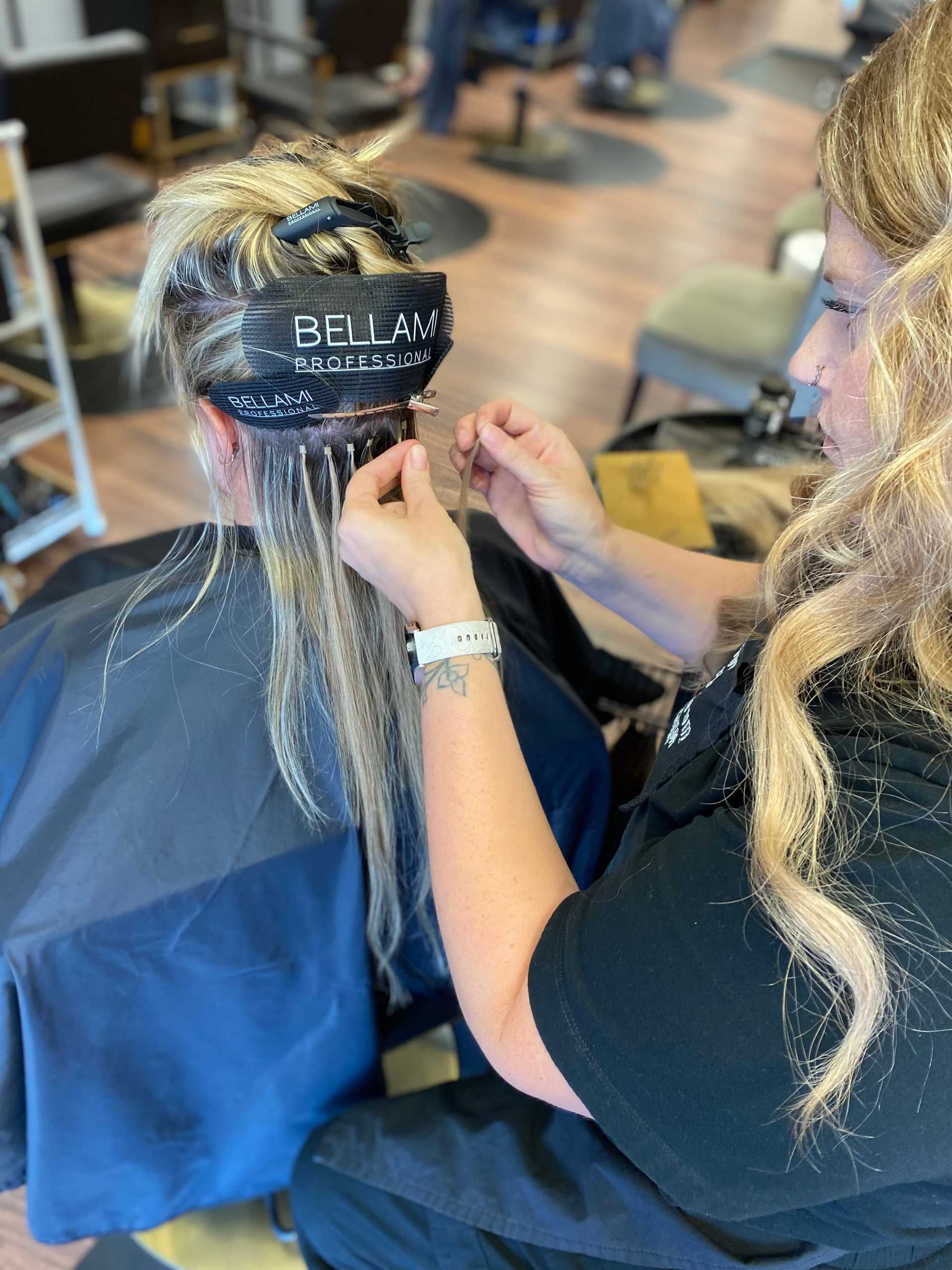 Hairdresser applying extensions to a client's hair in a salon.