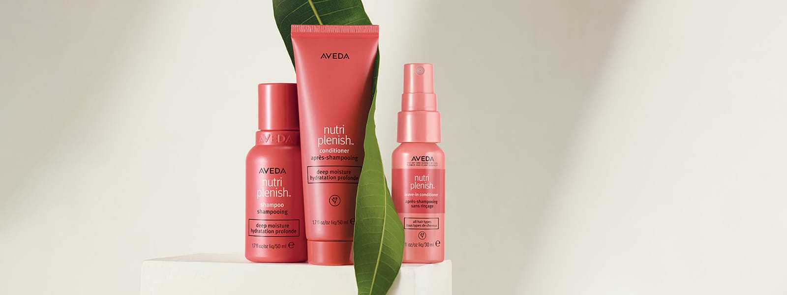 Aveda Nutriplenish hair products displayed on a pedestal with a green leaf backdrop.