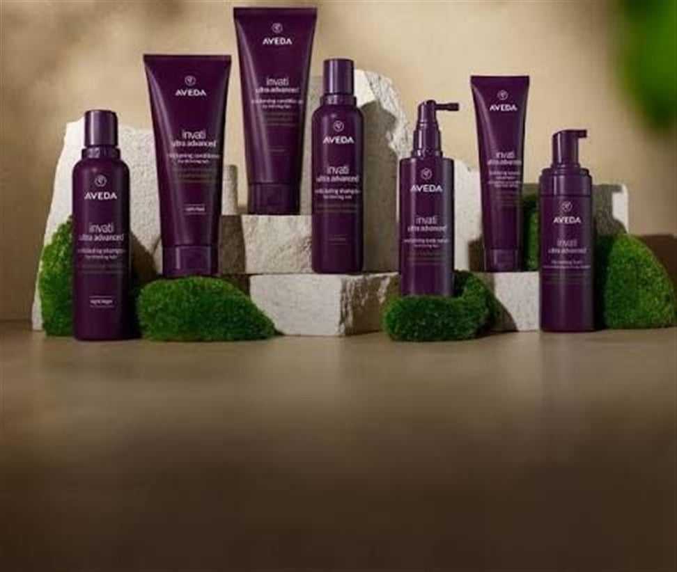 Aveda hair care products on display with rocks and moss in a natural setting.