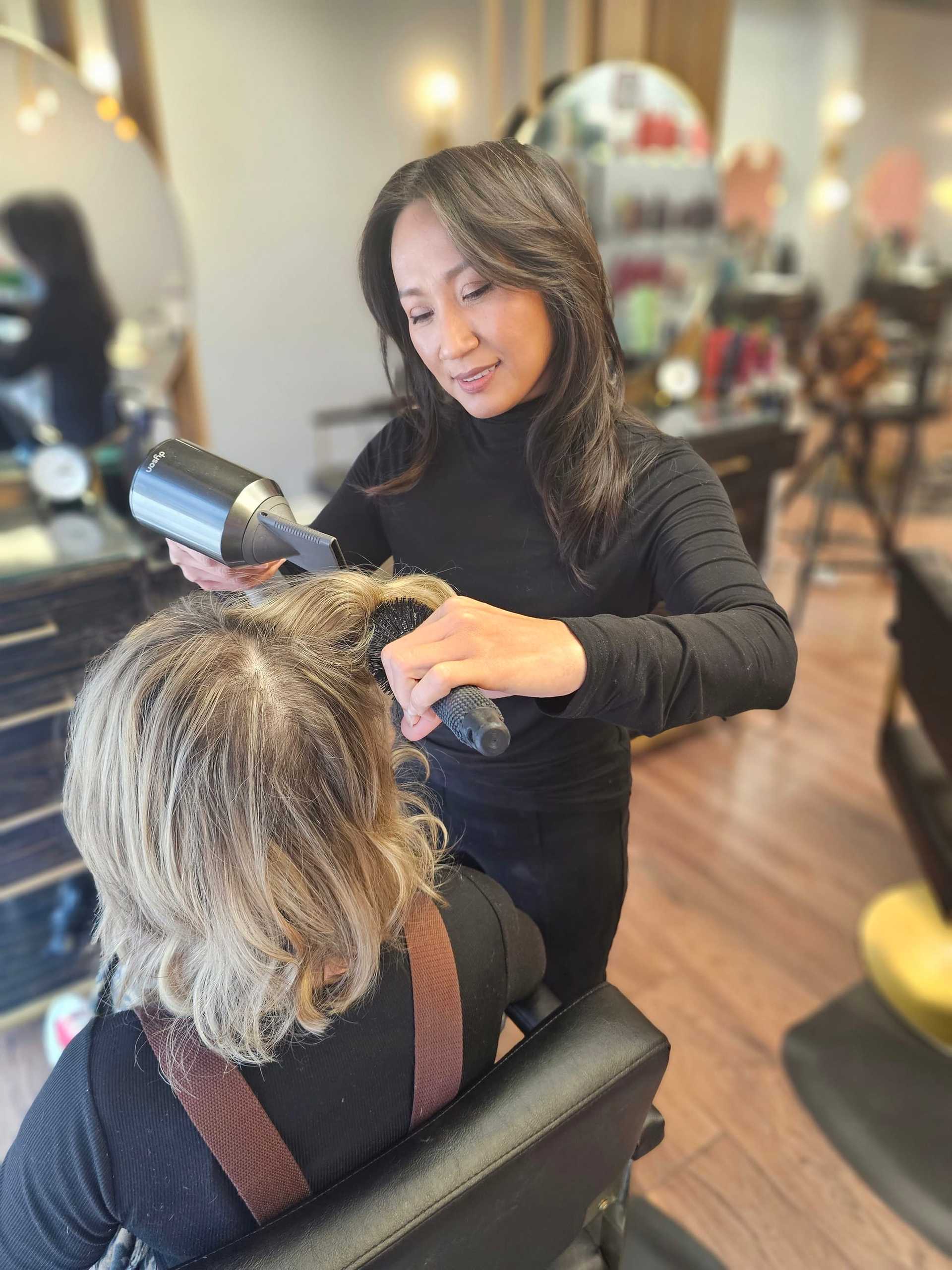 Hair stylist blow-drying a client's hair in a salon.