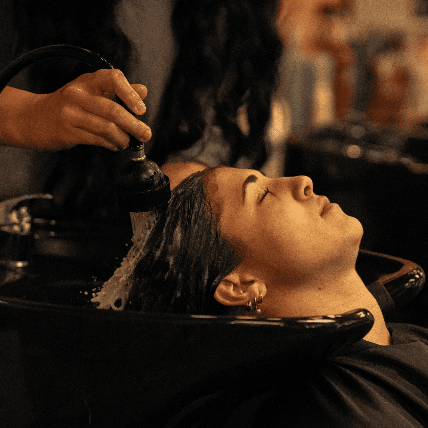 Hair salon scene: person getting a hair wash at a basin, eyes closed, enjoying the treatment.